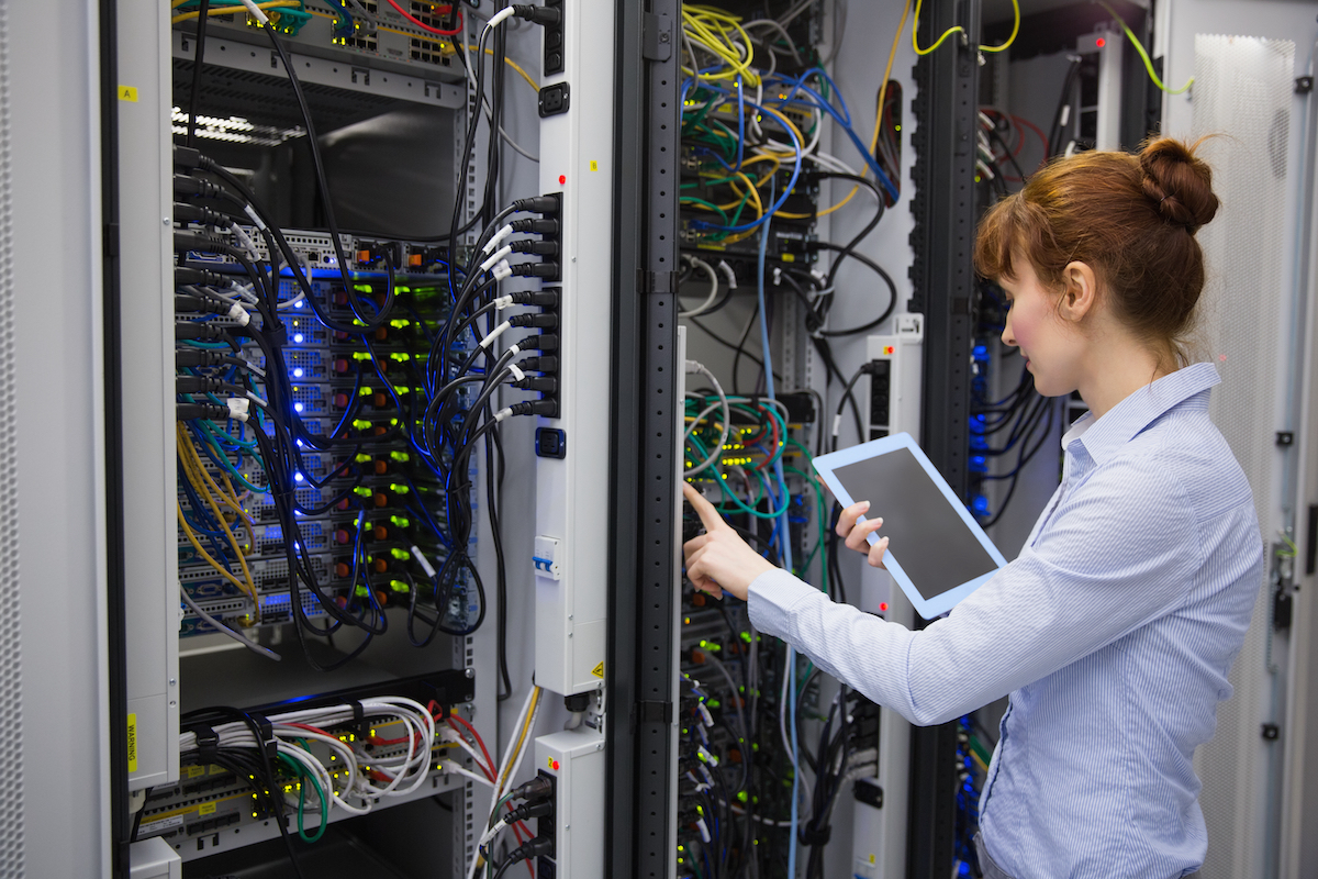 Secure server room with female technology specialist assessing hardware with a mobile device