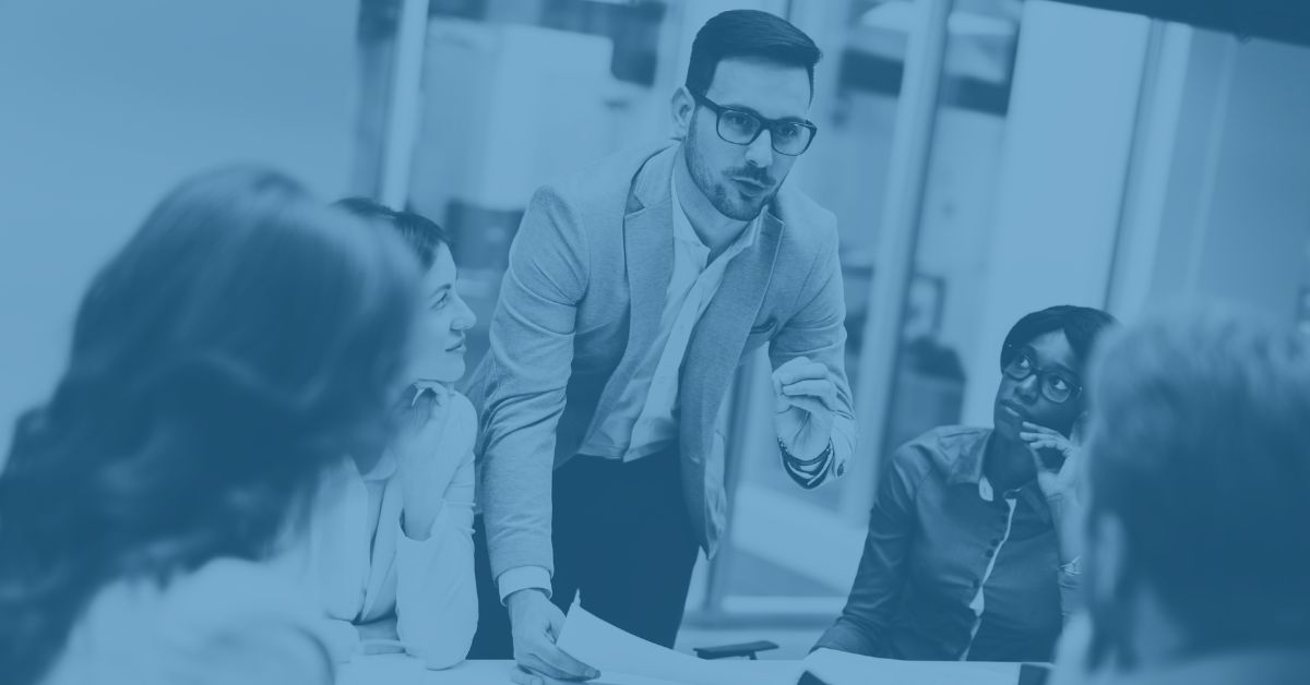 Professional EstesGroup project management team collaborating around a conference table with laptops, documents, and Epicor ERP system displays.